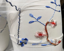 Load image into Gallery viewer, Close up view of the white blue embroidered mesh shorts to show the details of the embroidery