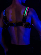 Load image into Gallery viewer, Rear view of model wearing a black harness with glowing blue, green and red straps against a dark background
